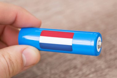 Hollanda bayrağı çıkartması olan bir adamın elinde şarj edilebilir Li-ion bataryası. Hollanda 'da lityum pilleri üretin