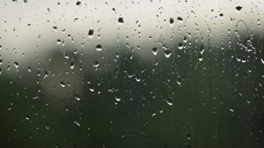 Pencere camındaki su damlacıklarına yakın çekim. Dışarıda yağmur yağıyor, damlalar düşüyor.