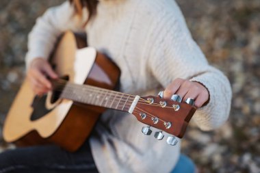 Kız akustik gitarı akort ediyor. Sonbahar parkında gitar akort eden bir müzisyenin elleri kapalı.