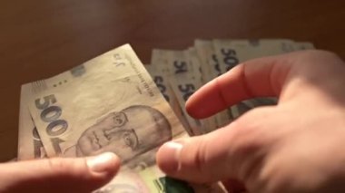 Ukraynalı 500 Hryvnia banknotunu sayan bir adamın yavaş çekim videosu. Masada büyük bir miktar Ukrayna Hryvnia faturası var, büyük bir alışverişe hazırlanıyor.