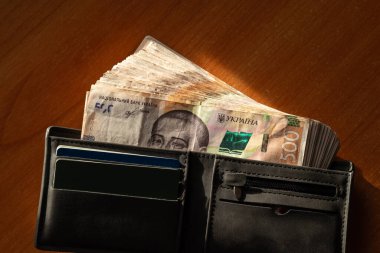 Güneş ışığının altındaki ahşap masada, siyah cüzdanda 500 hryvnianın banknotları, yakın çekim. Ukrayna parası, finans, zenginlik ve iyi kazanç kavramı