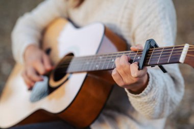 Gitarı çalan genç bir kadının ellerinde. Açık havada müzik çalmak, ekipman kaposu kullanmak.