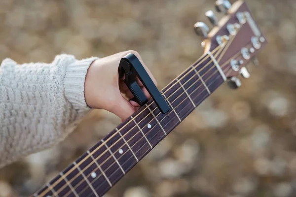 Female hand holding guitar and capo while playing in nature. Using special equipment to practice musical instrument