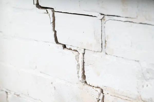 Crack on the white brick wall. Concept of ruining building errors while building structures, deterioration of building
