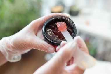 Profesyonel spa maskesini plastik kapta kozmetik uzmanının ellerine bırak. Güzellik salonunda profesyonel maskeli cilt bakımı