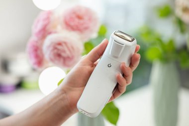 Profesyonel bir kozmetik uzmanının elindeki yüz masajı aracı, yakın plan, arka planda çiçekler. Vücut ve cilt bakımı için profesyonel bir araç