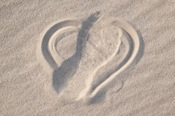 Shape of heart drawn on the sand, shoe print on it, close up. Concept of lost love, broken heart, bad emotions