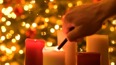 Noel ışıklarının arka planında mum yakmak. Çakmak tutuşturan adam kırmızı ve beyaz mumlar kullanmış. Arka planda güzel bulanık noel ışıkları var.