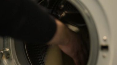 Erkek, kirli çamaşırları yıkamak için çamaşır makinesine koyuyor. Çamaşır, çamaşır, günlük rutin işler, ev işleri.