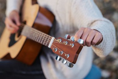 Dişi gitarist müzik aletinin tellerini tamir ediyor, yakın çekim. Serin bir sonbahar gününde doğada gitar çalmak.