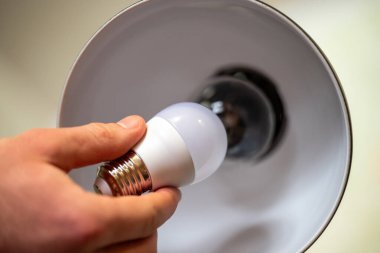Erkeğin elindeki beyaz LED ampulü, lambanın yanında parlak bir ampulle tutuyor. Yıldırımı değiştirmek, enerji verimliliği kavramı.
