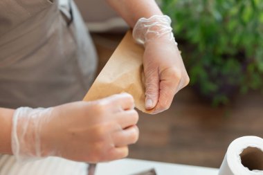 Tıbbi eldivenli kadın eli kâğıt zarf açarken yakın çekim. Gri üniformalı kozmetik bilimci onu açmak için kozmetik aletlerle dolu kağıt torba yırtıyor.