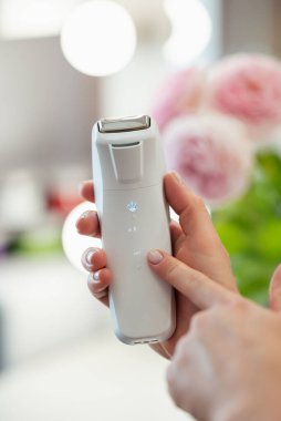 Kozmetik uzmanının elindeki profesyonel yüz masajı aleti, yakın plan, arka planda pembe çiçekler. Vücut ve cilt bakımı aracı, spa prosedürü kavramı