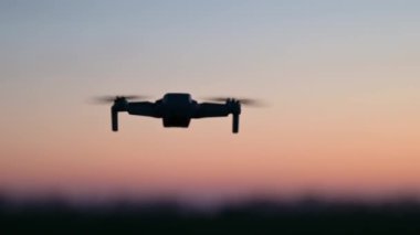 İnsansız hava aracı akşamları kırsal alanda uçuyor. Uçan küçük kuadkopter dron silueti, tarımsal alandaki mahsulleri denetliyor.