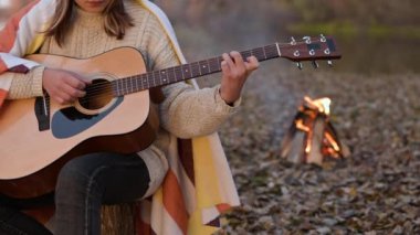Şenlik ateşiyle gitar çalan genç ve güzel bir kız. Sonbahar ormanında kamp yapmak, sakin bir akşam, tek başına gitar çalmak.