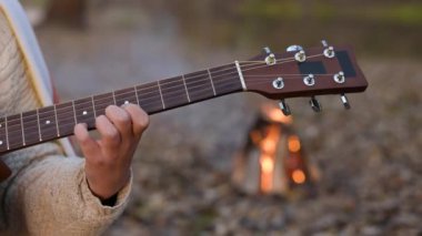 Gitar çalan bir kızın elleri, arka planda şenlik ateşi. Yaz tatili, ormanda kamp yapmak, doğada gitar çalmak.