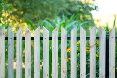 Arka planda güneşli bir yaz gününde bahçeli ahşap çit. Kırsal kesimde yeni yapılmış çitler, el işçiliği ile ev dekorasyonu ve geliştirme