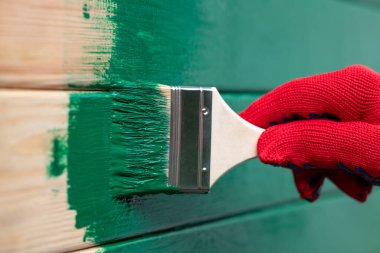 Duvarı yeşile boyuyorum. Fırçalı bir evin ahşap duvarına boya sürüyorum.