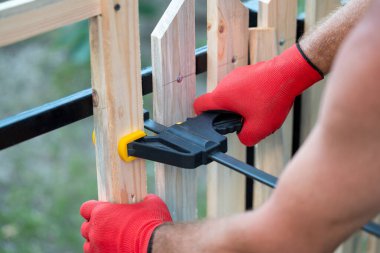 Metal çerçeveli ahşap çitler inşa ediyor. Parantez kullanarak çitlere aynı mesafede tahta bağlayan bir adamın elleri