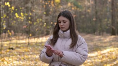 Sonbahar parkında telefonu kullanan kızgın genç kız. Genç bir kız birine kızgın, sonbahar ormanlarında yürürken bir arkadaşından mesaj almış.