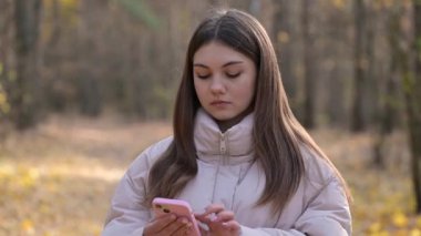 Genç liseli kız telefonda bazı bilgileri okuduktan sonra sinirlenir ve sinirlenir. Sonbahar ormanlarında ceketiyle yürüyen genç bir kız telefonla sinirli ve agresif bir şekilde iletişim kuruyor.