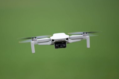 Kameralı uçan bir dronun ön görüntüsü. Yeşil alanın arka planında uçan küçük tüketici kuadkopteri