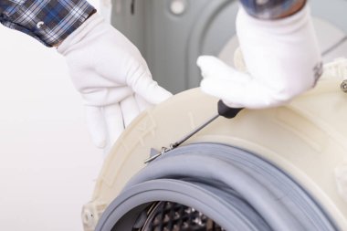 Servis merkezinde çamaşır makinası tamir ediyorum. Tamirci çamaşır makinesinin varilini sökmüş, tornavidayla lastik conta çıkarmış.