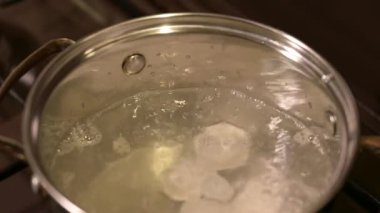 Evde mantı pişiriyorum. Etli dondurulmuş hamur köftelerini kaynayan suya koyup kaşıkla karıştırmak.