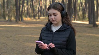 Ormanda koşan kız mesaj alır ve okurken kibirli hisseder. Ormanda koşan bir kız telefonundan mesaj okumak için duraklıyor, kendine güven ve aşağılama yayıyor.