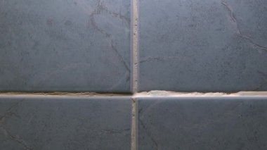 Adam, zayıf fayans döşemesini yanlış hizalama ve boşluklarla eleştiriyor. Bir adam duvardaki kötü fayansların kalitesini kontrol eder. Düz olmayan bir yüzeye dikkat çeker. Kötü döşeme kurulumu aşikardır.