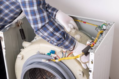 Cihaz iç organları üzerinde çalışan teknisyenli çamaşır makinesinin onarım servisi. Bir teknisyen çamaşır makinesini tamir eder, iç organları inceler ve servis ortamında kablo döşeyebilir.