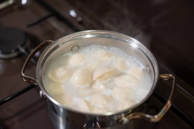 Sıcak bir mutfak ortamında, ocağın tepesinde hamur köftesi kaynatmak. Hamur köfteleri ocağın üstünde kaynıyor, sıcak bir mutfak atmosferinde buhar ve kabarcıklar yaratıyor.