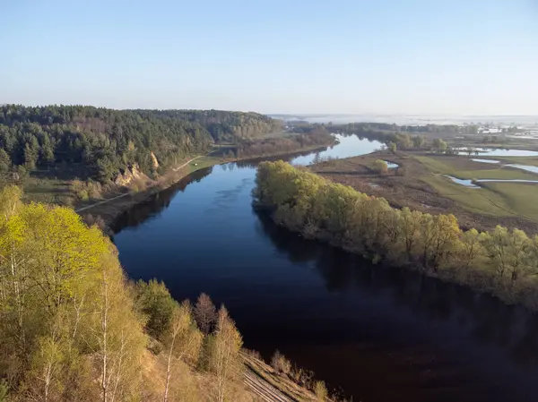 Bahar sabahı yemyeşil ve açık gökyüzü sularla doldu. Sabah ışığı, canlı bahar yaprakları arasında akan bir nehri yansıtıyor. Doğanın güzelliğini vurguluyor.