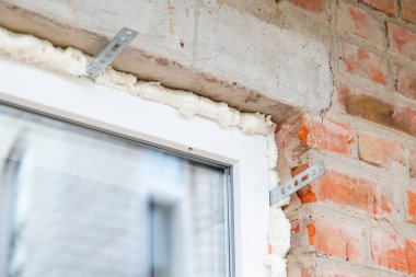 Pencere çerçevesi yalıtım köpüğü ve inşaat malzemelerini ön plana çıkarıyor. Bir binaya kurulmuş yeni pencere, yalıtım ve destek parantezlerinin yerleştirildiğini, bitirmeye hazır olduğunu gösterir