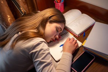 Ders çalıştıktan sonra yorgun genç kız kitapların üzerinde dinleniyor. Matematik okuduktan sonra kitapların ve defterlerin üzerinde yorgun yatan genç kız.