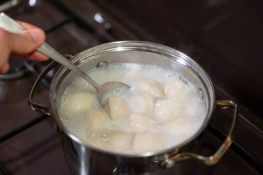 Kabaran su kabında hamur tatlısı karıştırmak. Kaynar suyla dolu bir tencerede beyaz, yuvarlak hamur köftelerini karıştırıp pişirme sürecini gösteren yakın plan bir kaşık.