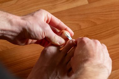 Adam manikür makasıyla ayak tırnağını kesiyor. Tırnağını manikür makasıyla kesen bir adam.