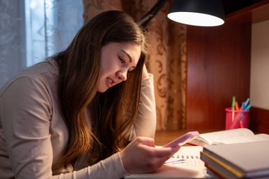 Öğrenci çalışırken ve telefonuna bakarken üzgün. Masasında oturan genç bir kadın elinde bir telefonla ona endişeli bir ifadeyle bakıyor. Umutsuzluğa kapılmış.