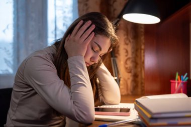 Öğrenci büyük bir ev ödevinden dolayı yorgun. Genç bir kadın, kafası ellerinin arasında bir masada oturuyor. Yorgun ve yoğun bir iş yükü altında.