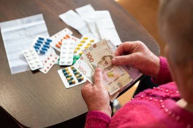 Büyükannem ilaç aldıktan sonra hryvnias tutuyor. Yaşlı kadın, Ukrayna 'da yüksek sağlık giderleri gösteren haplar aldıktan sonra parasını inceliyor.