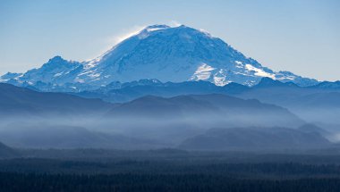 A view of Mount Rainier near Seattle with layers of foothills shrouded in mist in front clipart