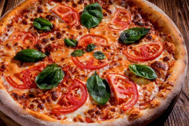 Delicious fragrant pizza with mozzarella, tomatoes and basil with tomato sauce on woden background.