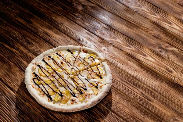 Sweet delicious pizza with apple, cinnamon, chocolate on wood background. Pizza dessert. Top view. Copy space.