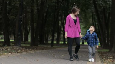 Genç anne oğlunun elini tutuyor ve okula gidiyor. Anne ve oğlu okul bahçesinde yürüyor..