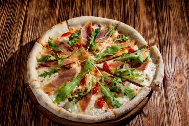 Pizza with jamon and prosciutto, mozzarella, cherry tomatoes, arugula and parmesan on a wood background. Italian cuisine