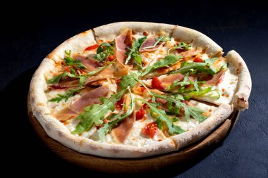 Pizza with jamon or prosciutto, mozzarella, cherry tomatoes, arugula and parmesan on a black background. Italian cuisine