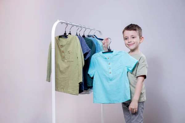 Little Stylish Preschool Boy Staiding Clothes Rack Holding Shirt Demonstrates — 图库照片