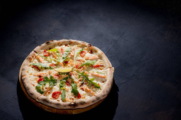 Пицца с лососем, моцареллой, помидорами черри, аругулой, лимоном и пармезаном. Итальянская кухня. На черном фоне. Свободное место для текста. Вид сверху
