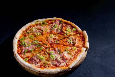 Delicious pizza with mozzarella cheese, ham, leeks on a tomato base on black background.