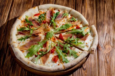 Pizza with jamon and prosciutto, mozzarella, cherry tomatoes, arugula and parmesan on a wood background. Italian cuisine